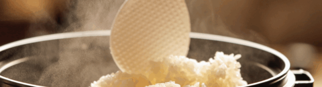 しゃもじで熱々のご飯をすくい上げる瞬間。鍋から立ち上る湯気が見える