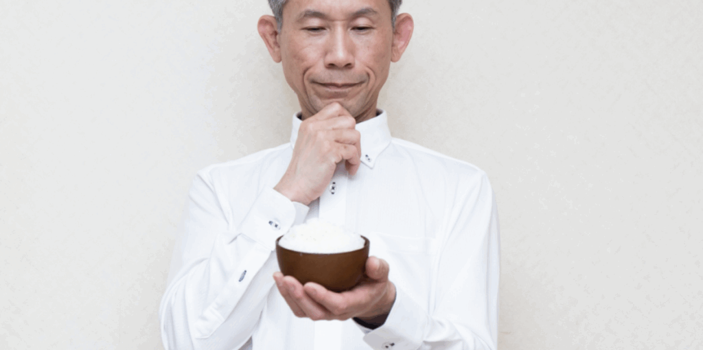 白いシャツの中年男性が小さな茶碗のご飯を考え込むように見つめている