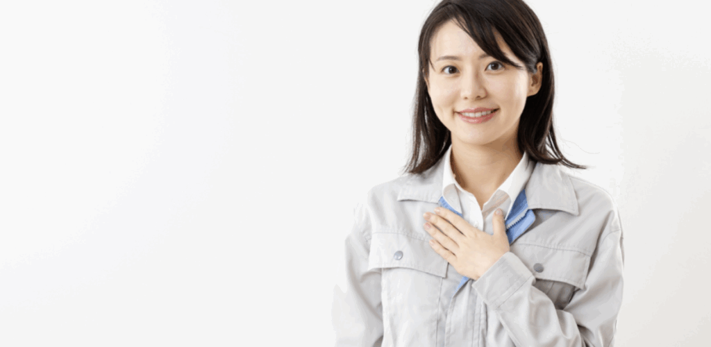 作業服を着た女性スタッフが胸に手を当てて笑顔で立っている
