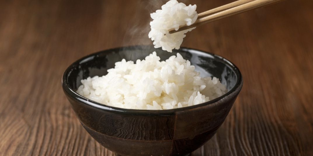 湯気の立つ白米を箸ですくう瞬間のアップ。艶やかで粒立ちの良いご飯の炊き上がりイメージ