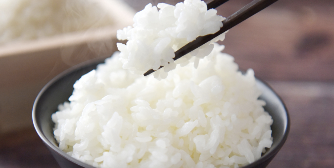 茶碗の白米を箸でつまみ上げた湯気立つご飯のクローズアップ